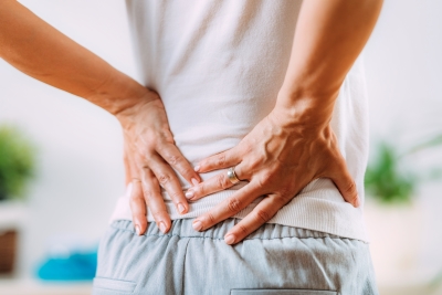 Woman holding her aching lower back, which can be relieved with heat plasters