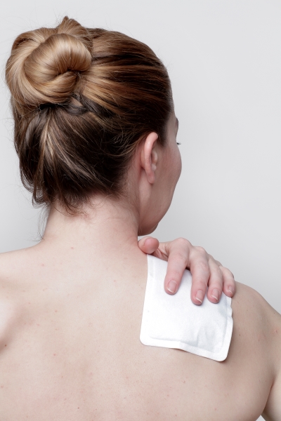 Woman using a heat plaster for pain relief in the shoulder