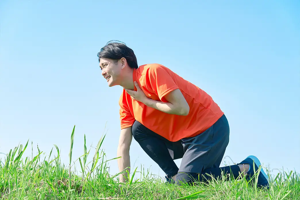 Call the emergency services immediately in case of shortness of breath or other severe symptoms after an insect sting A young man kneels on a lawn with shortness of breath and holds his chest